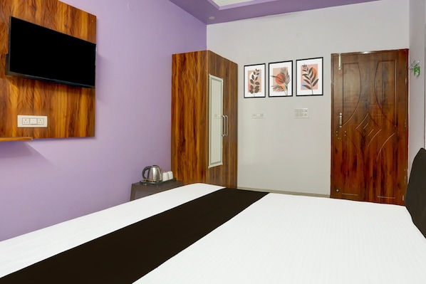 A bedroom with a bed, a television mounted on the wall, a wooden wardrobe, and a door with a decorative handle.