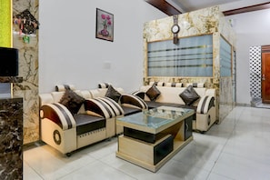 A living room with a sofa set, a glass coffee table, and a wall-mounted clock.