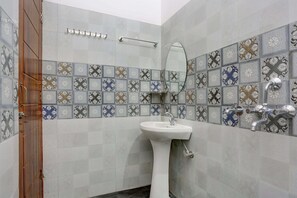 A bathroom with a white pedestal sink, a mirror, a towel rack, and a shower with a chrome faucet.