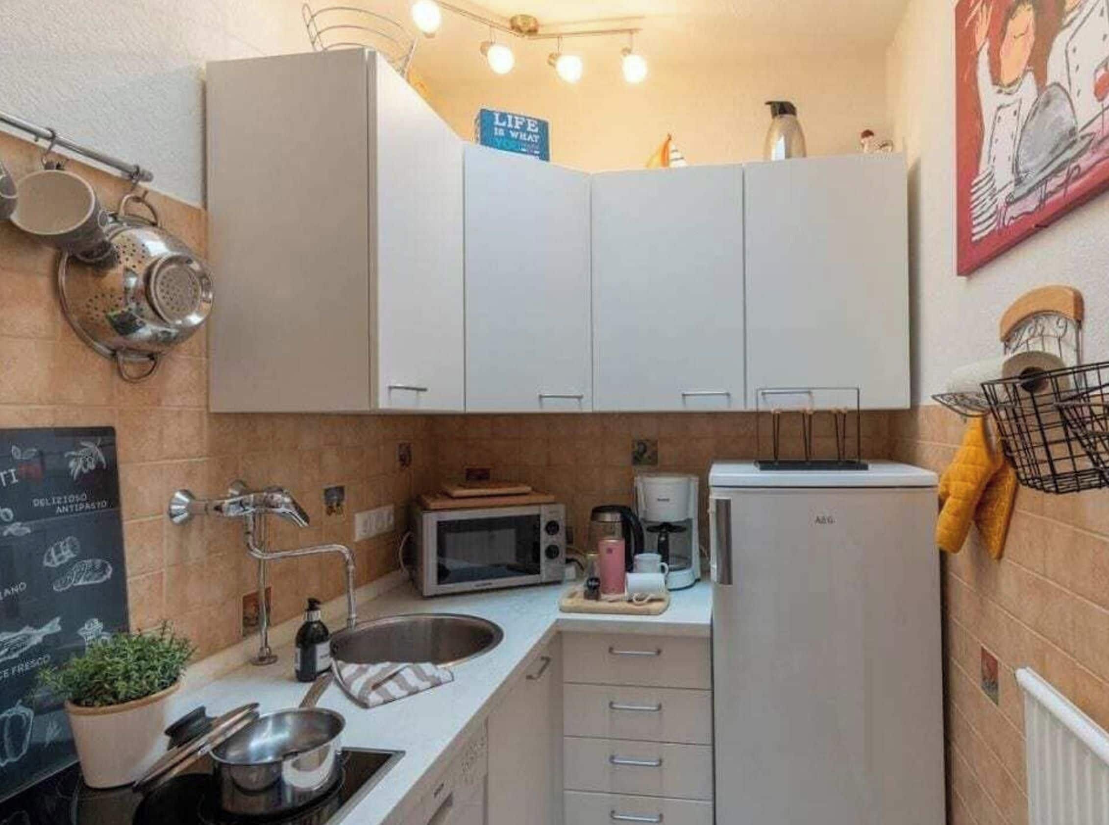 A compact kitchen with white cabinets, a microwave, a coffee maker, and a small sink.