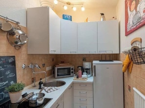 A compact kitchen with white cabinets, a microwave, a coffee maker, and a small sink. - Holiday Apartment With 1 Bedroom (Heiligenhafen)
