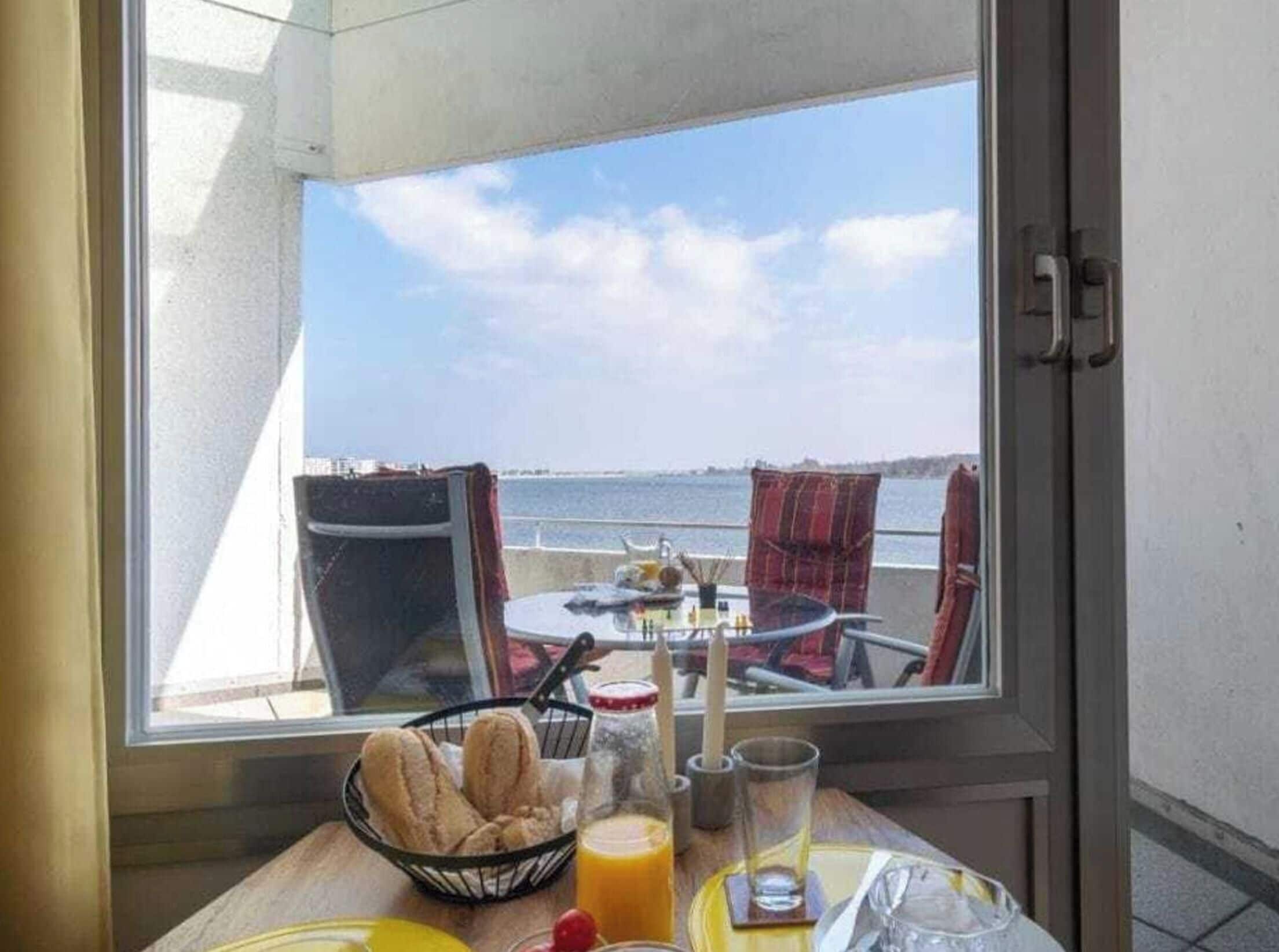 A dining table with breakfast items, a glass of orange juice, and a view of the sea through a window.