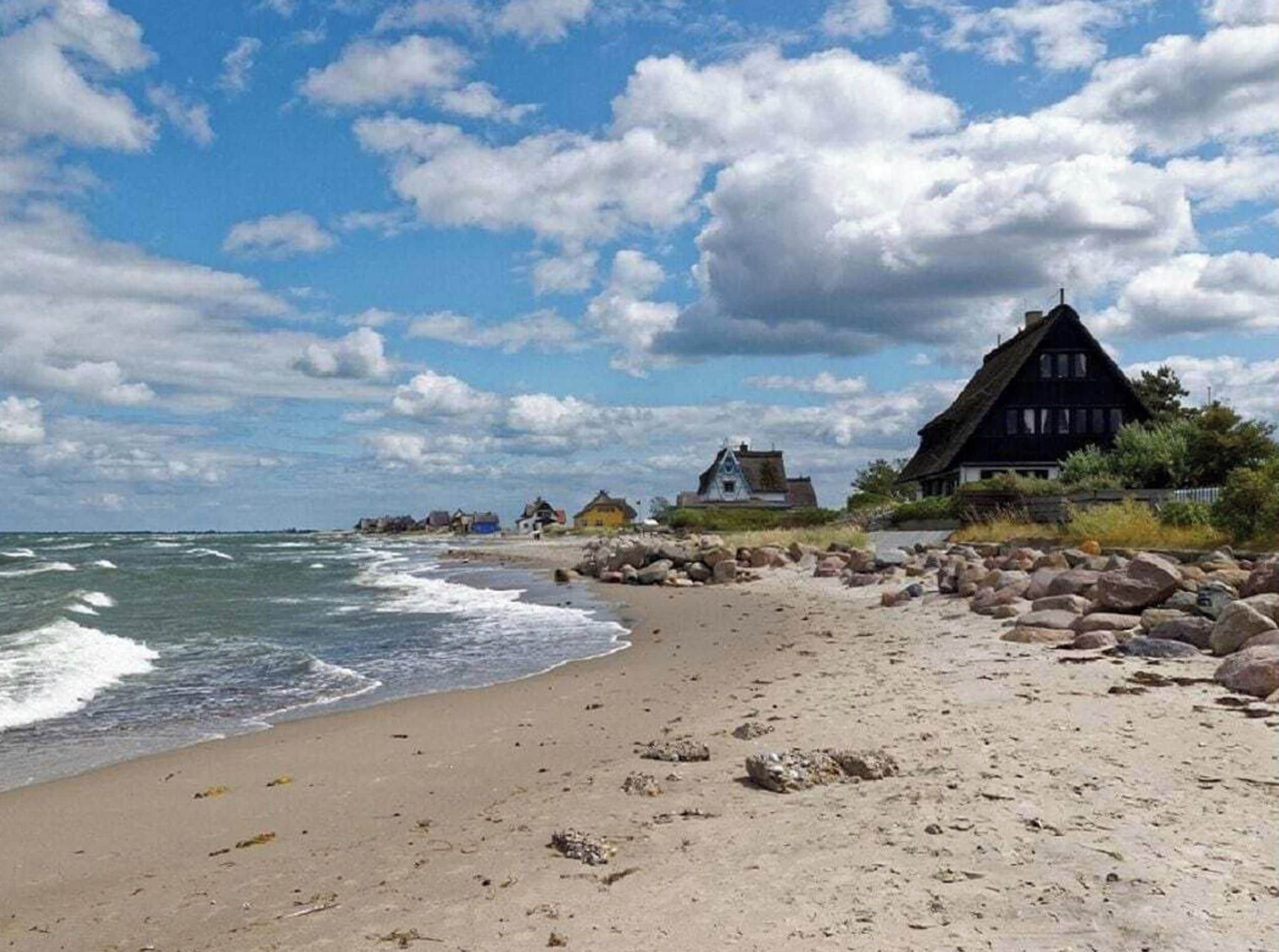 A beach with a row of houses, some with thatched roofs, and a rocky shoreline.