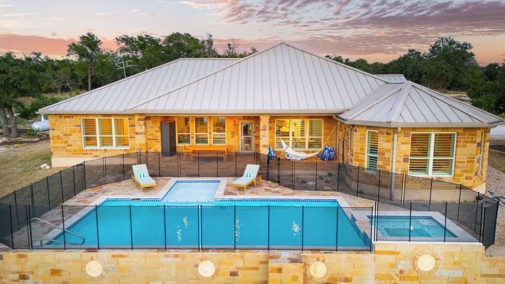 Une maison avec une piscine, deux chaises longues et un hamac.