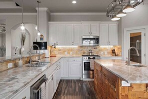 A modern kitchen with white cabinets, a central island, stainless steel appliances, and pendant lighting. - Solterra Hilltop | Pool | Grill + Endless Views! (Fredericksburg)