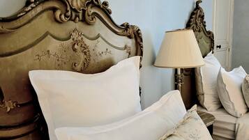 A bed with ornate headboard, white pillows, and a lamp on a bedside table.