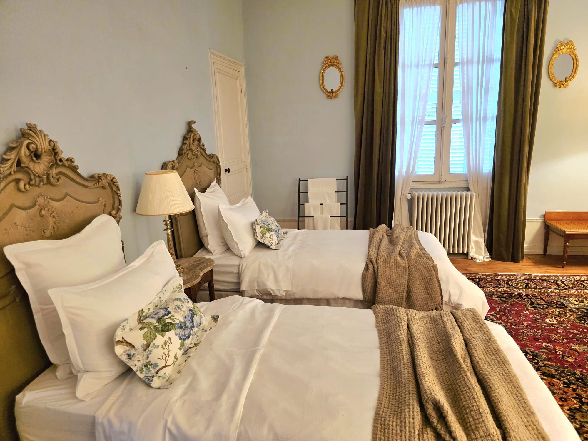 Habitación de hotel con dos camas, una mesita de noche, una lámpara, un radiador y una ventana con cortinas.