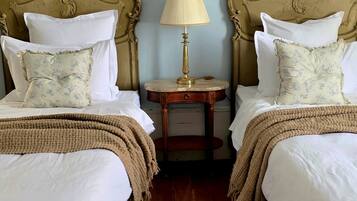 A room with two beds, a small table with a lamp, and a patterned rug.