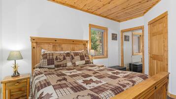 Une chambre à coucher avec une tête de lit en bois, une couvre-lit matelassée, une table de chevet avec une lampe et une fenêtre donnant sur des arbres.