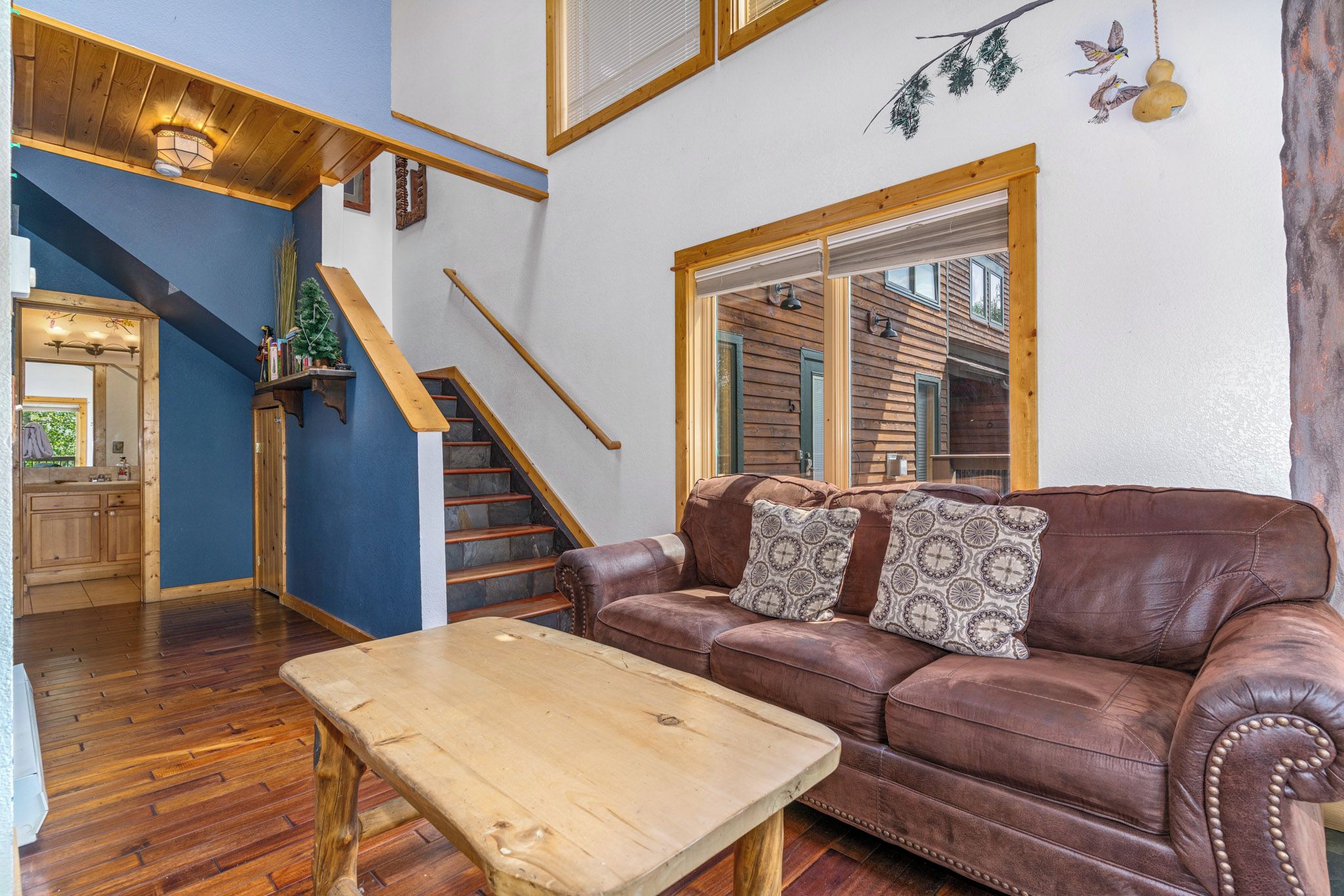 A cozy living room with a brown leather sofa, a wooden coffee table, and a staircase leading to an upper level.