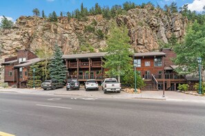 A lodge with a wooden exterior, multiple balconies, and a parking area with SUVs and a pickup truck. - Spacious 2-bedroom loft condo in downtown Estes Park - walk to restaurants/shops (Estes Park)