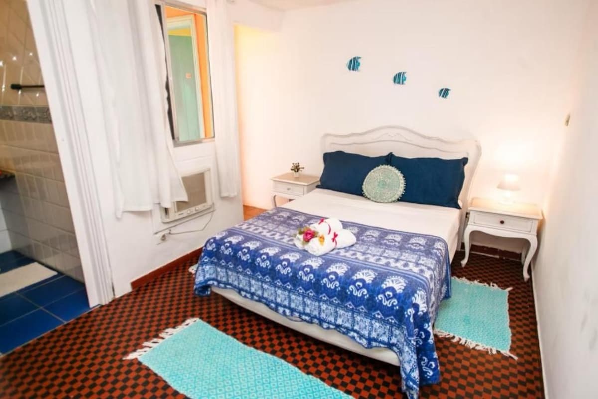 A bedroom with a bed, two bedside tables, a nightstand, a window with curtains, and a patterned floor.