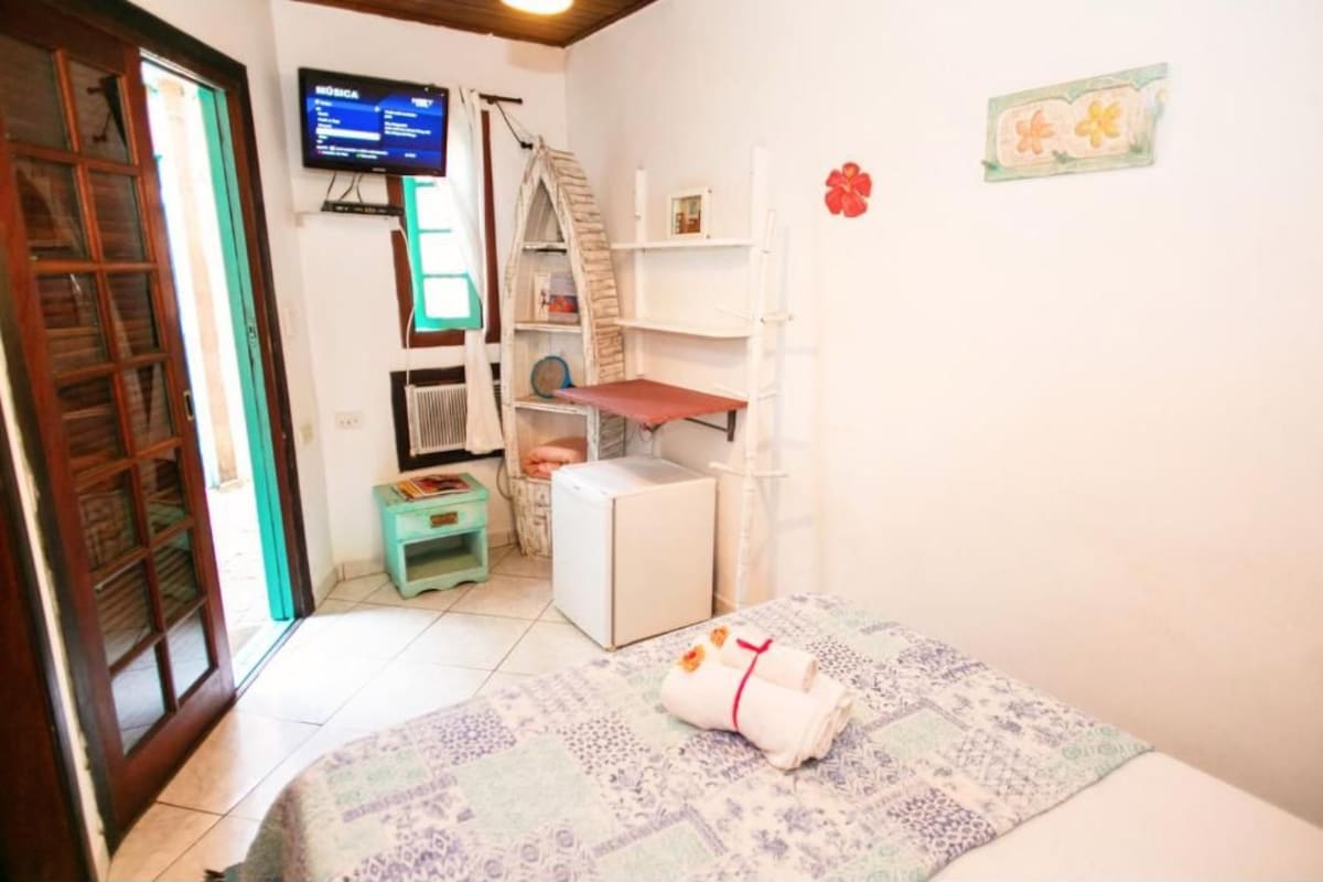 A room with a bed, a television, a small table, and a shelf with books.