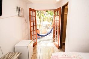 A room with a doorway leading to an outdoor area with a hammock and a table. - Canto das Laranjeiras Tombo  (Guarujá)