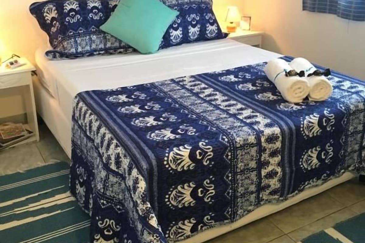 A bedroom with a bed, pillows, a nightstand, a lamp, and a floral artwork on the wall.