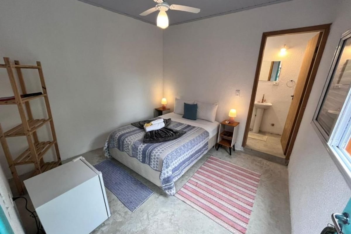 A bedroom with a bed, bedside tables, a wardrobe, a ceiling fan, a radiator, and a window.