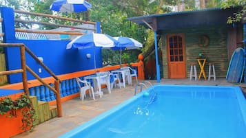 Piscina com deck de madeira, área de estar ao ar livre e guarda-sóis.