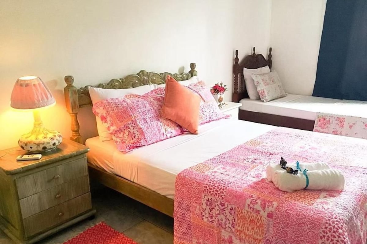 A bedroom with a bed, nightstand, lamp, and a red rug.