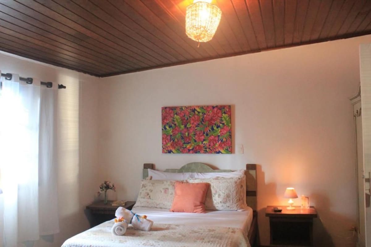 A hotel room with a bed, a nightstand, a lamp, and a floral painting on the wall.