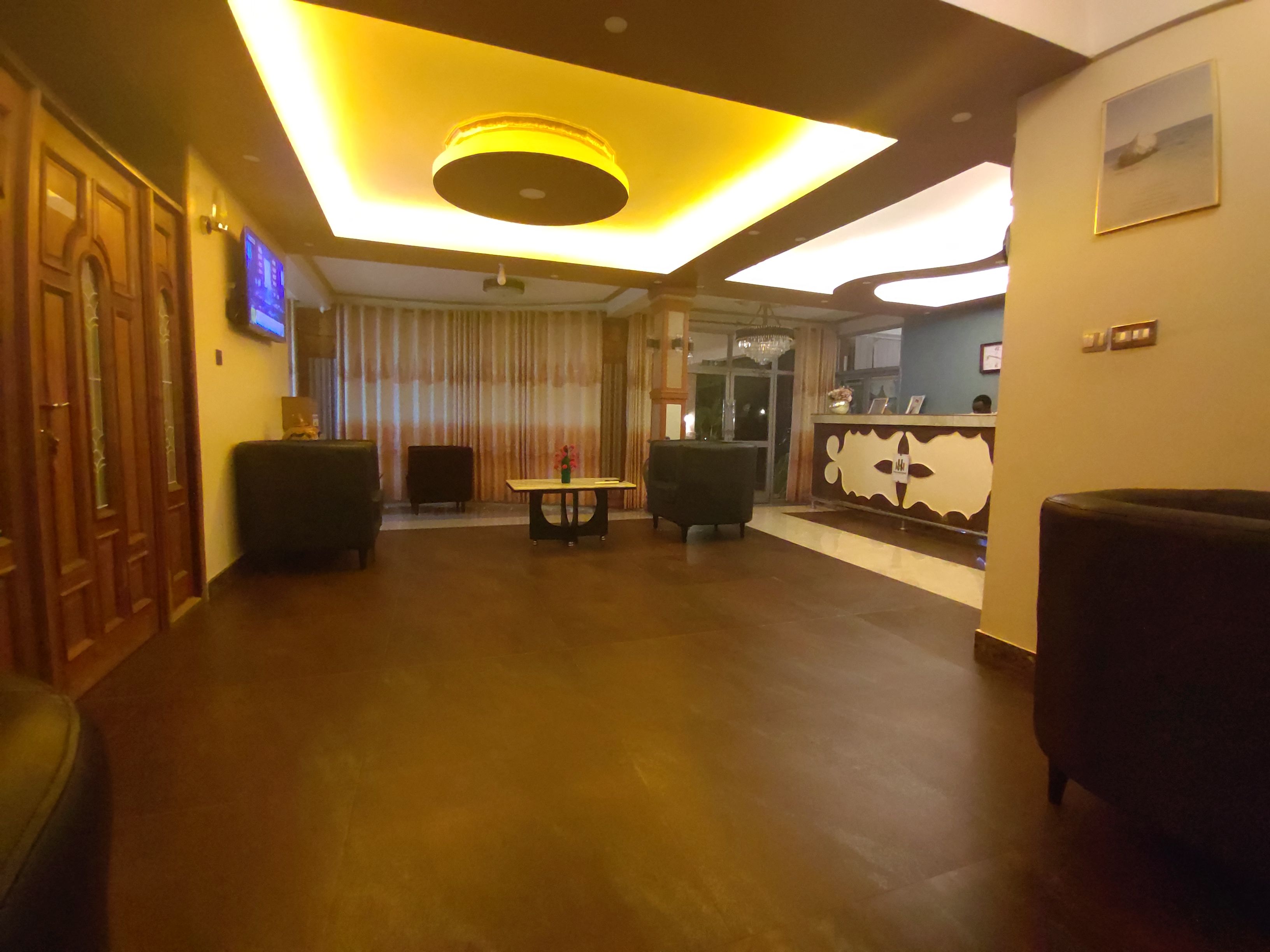 Een hotel lobby met een receptiebalie, een zithoek en een televisiescherm.