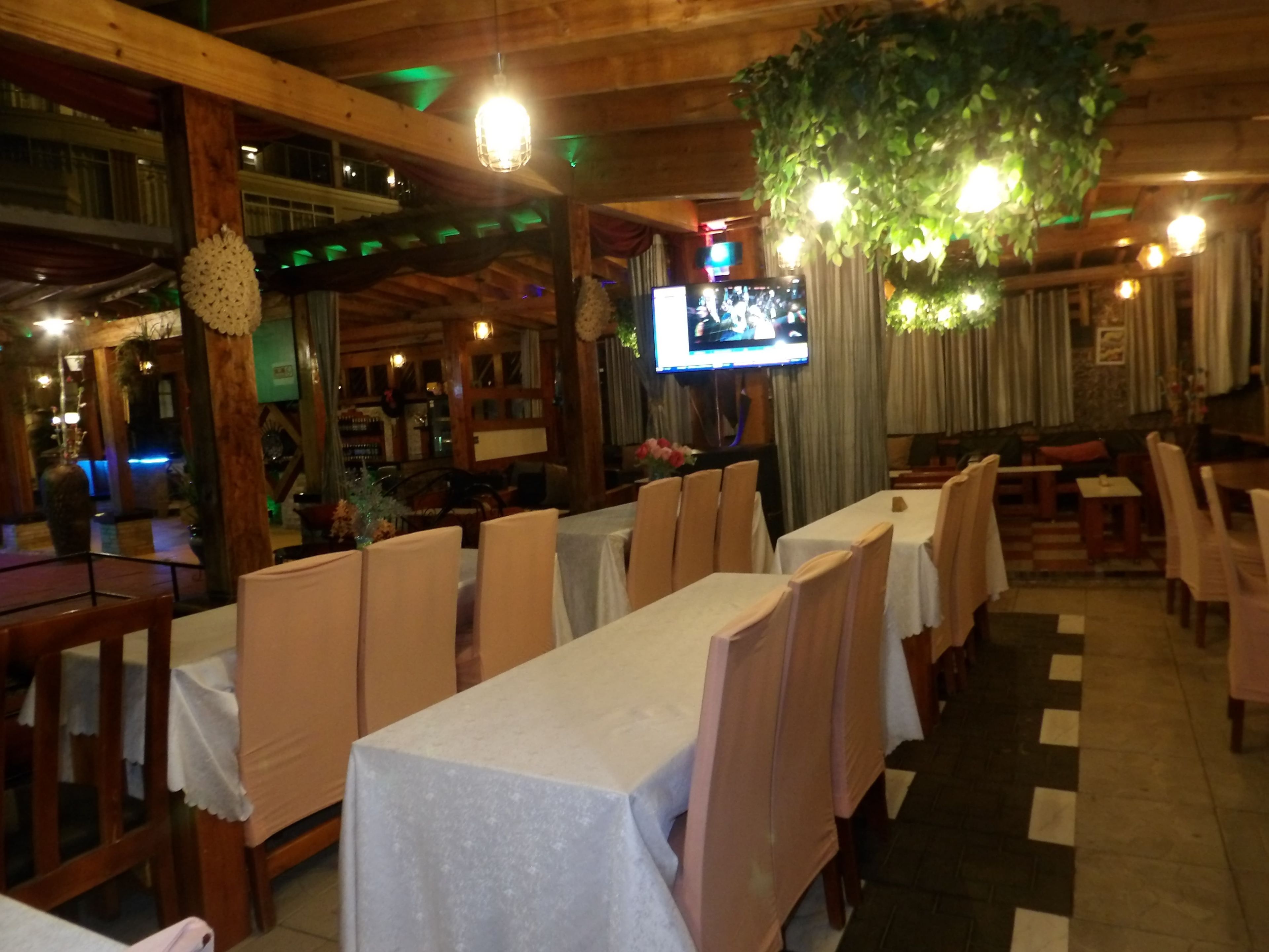 Een restaurant met lange tafels, stoelen en een aan de muur bevestigde televisie.