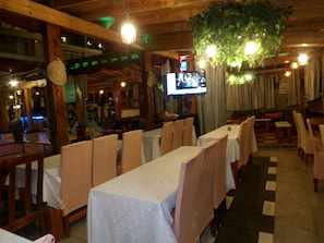 Un restaurante con mesas largas, sillas y un televisor montado en la pared.