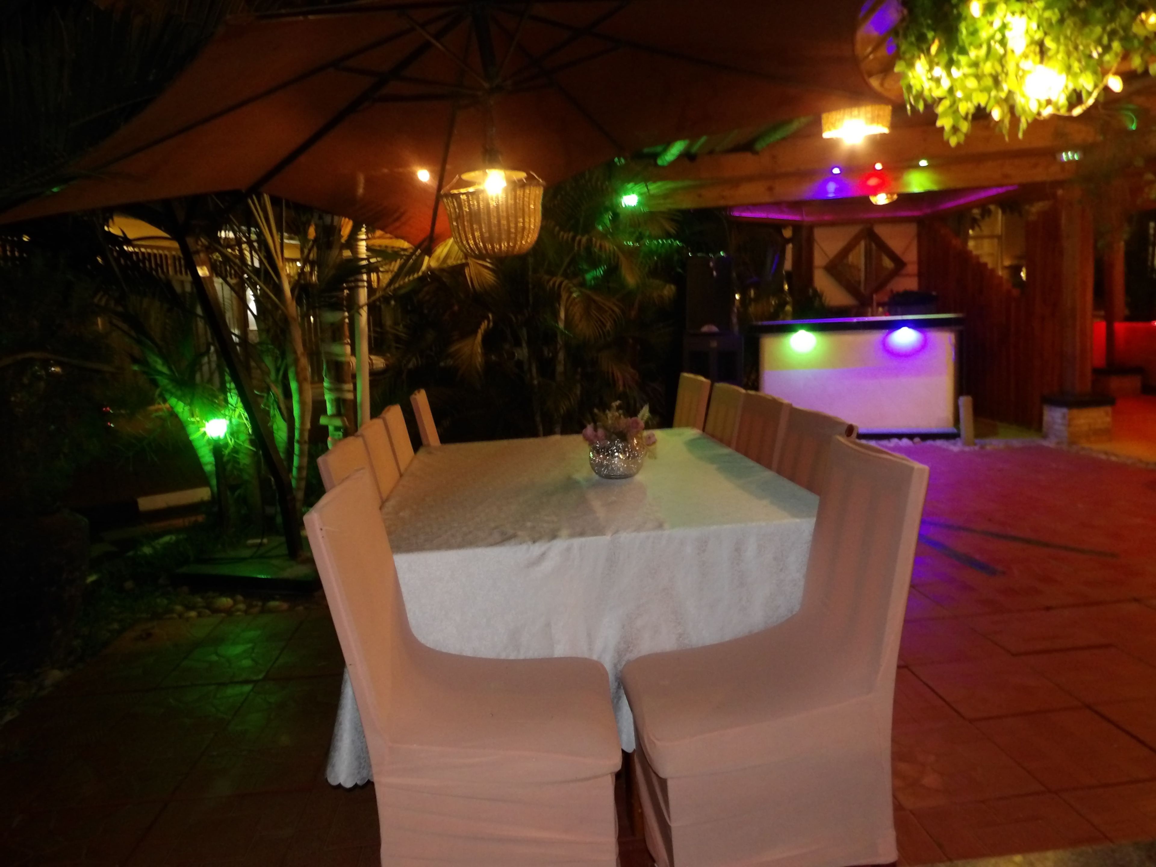 Un área de comedor al aire libre con una mesa y sillas, una lámpara colgante y una barra de fondo.