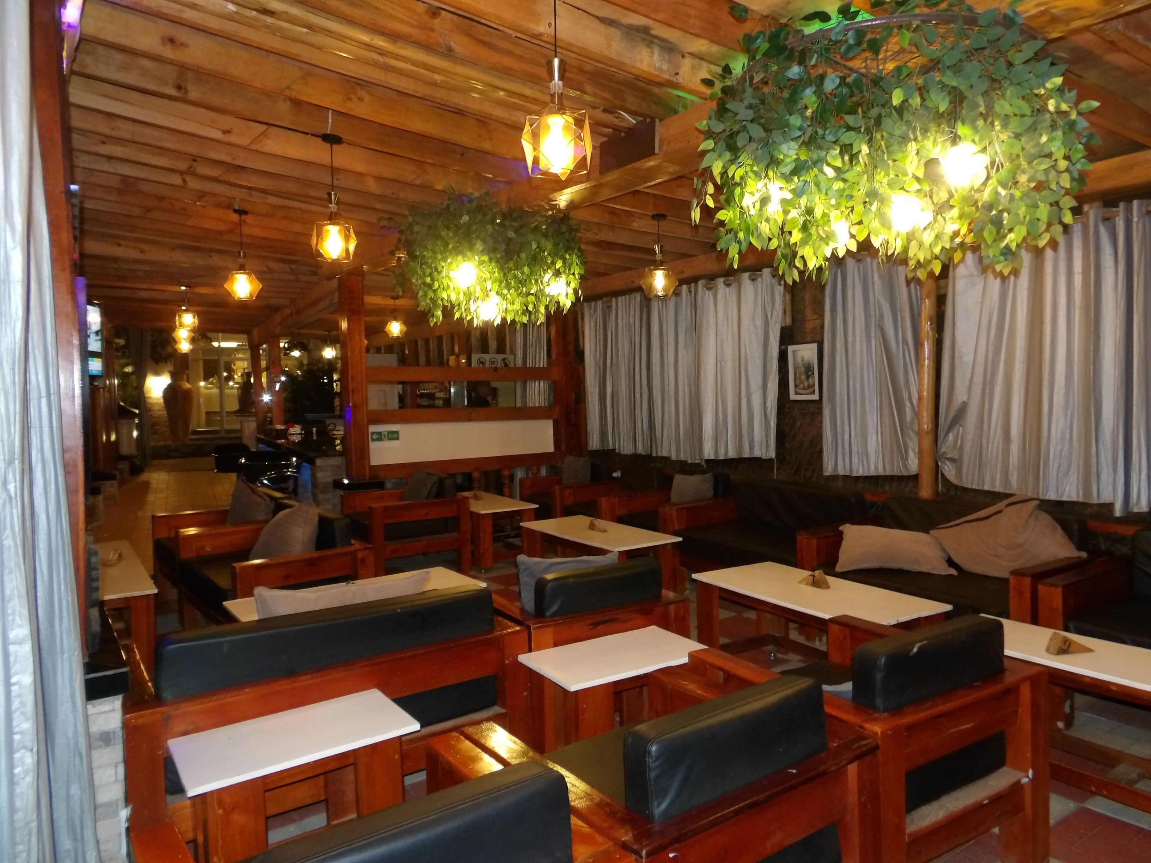 A restaurant interior with wooden tables and benches, hanging plants, and a warm ambiance.