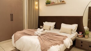 Ein Schlafzimmer mit Bett, Nachttisch, Kleiderschrank, einer Regalreihe mit Dekoration und einem Spiegel.
