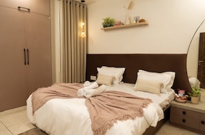 Ein Schlafzimmer mit Bett, Nachttisch, Kleiderschrank, einer Regalreihe mit Dekoration und einem Spiegel.