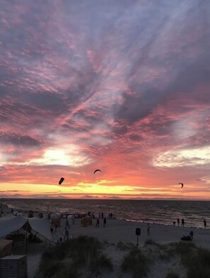 A beach with tents and people, and a sunset with clouds. - Steinwarder 7, Apartment "strandbude 33" (Heiligenhafen)