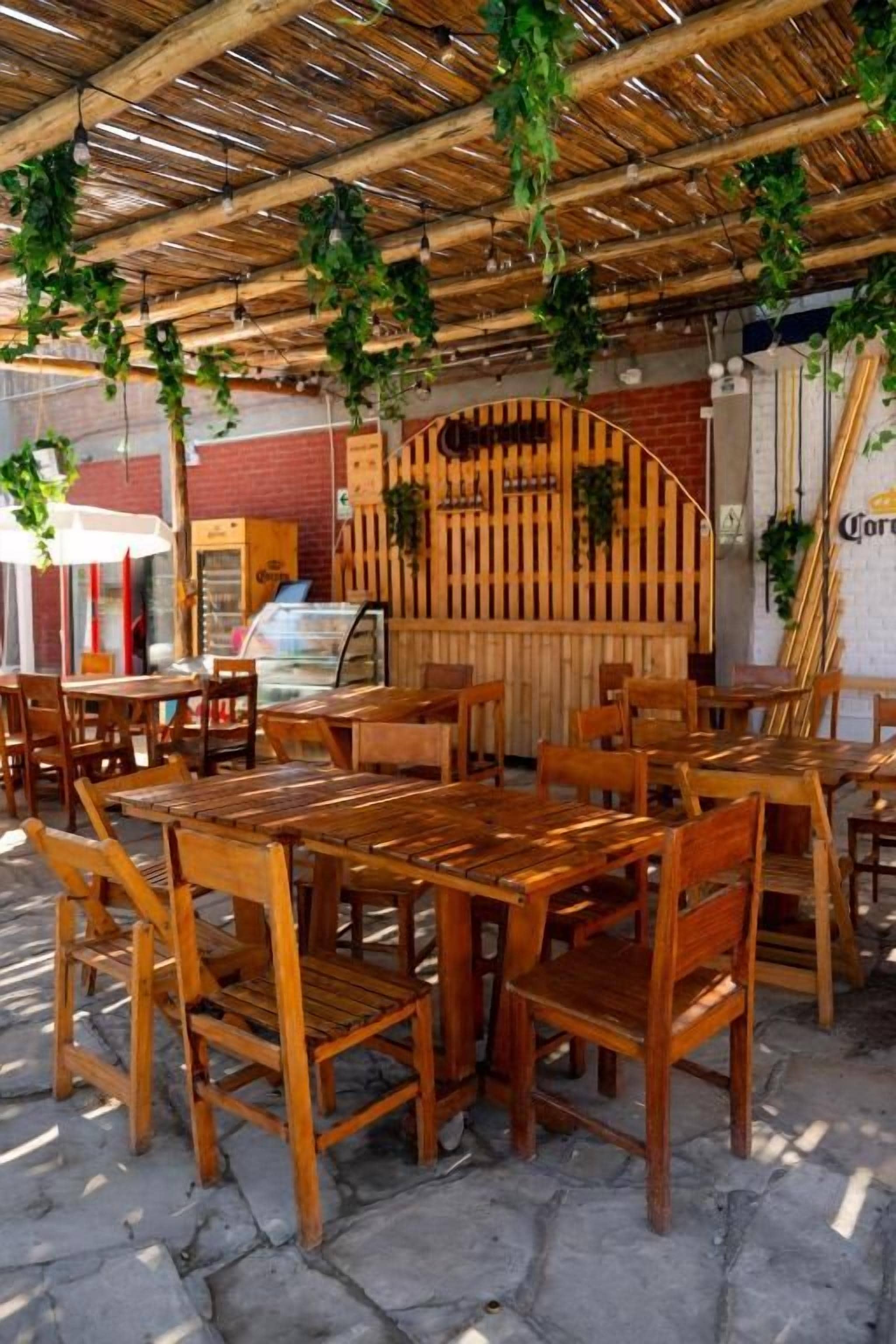An outdoor seating area with wooden tables and chairs, a brick wall, and hanging plants.