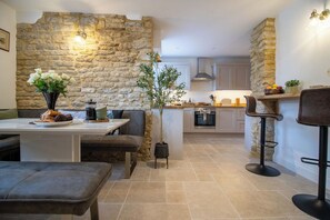A modern kitchen with stone walls, a dining area with a bench, and a bar with stools. - Belmont House - 4 bed, ensuites, private parking (Lincolnshire)