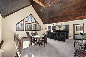 Ein geräumiges Zimmer mit hohen Decken, großen Fenstern, einem Essbereich mit Tisch und Stühlen sowie einer Küchenzeile mit Bar.