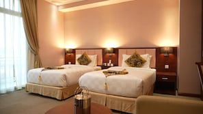 Een hotelkamer met twee bedden, een bureau, een stoel en een raam met gordijnen.