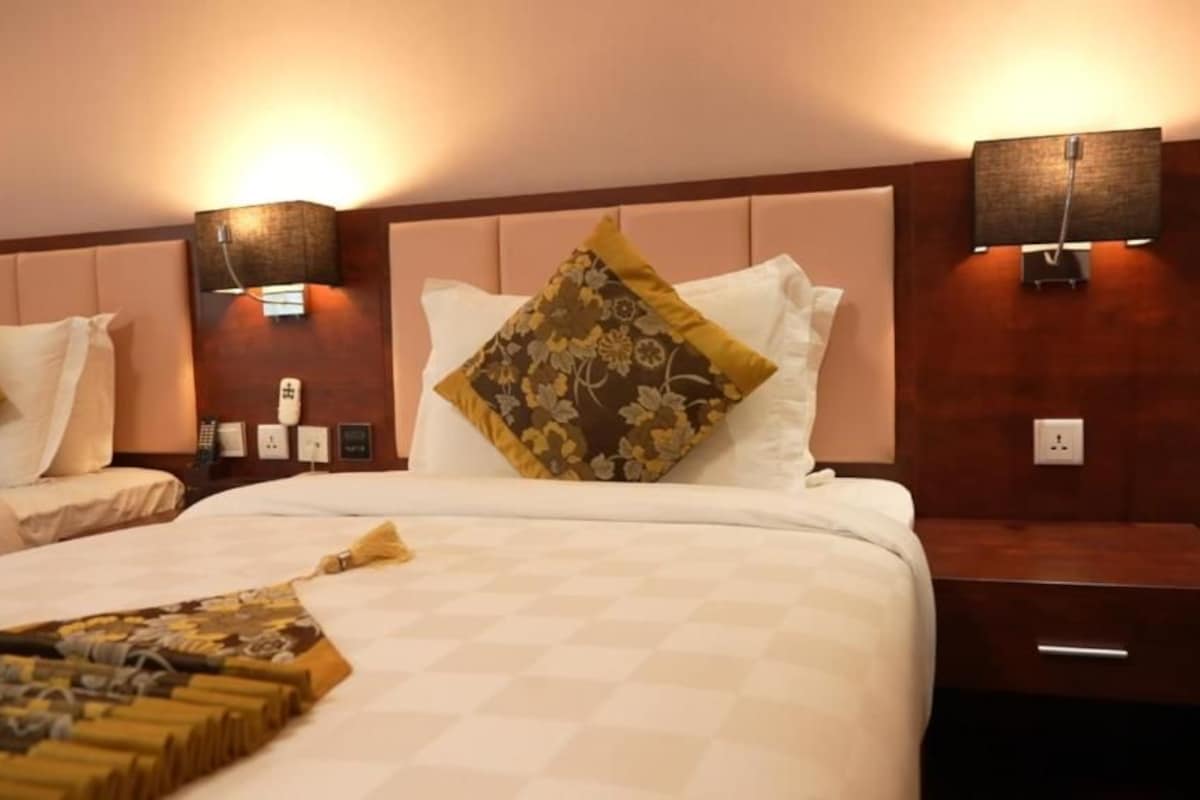 Een hotelkamer met twee bedden, elk met hoofdeinde, bedlampjes en een nachtkastje met een lade.