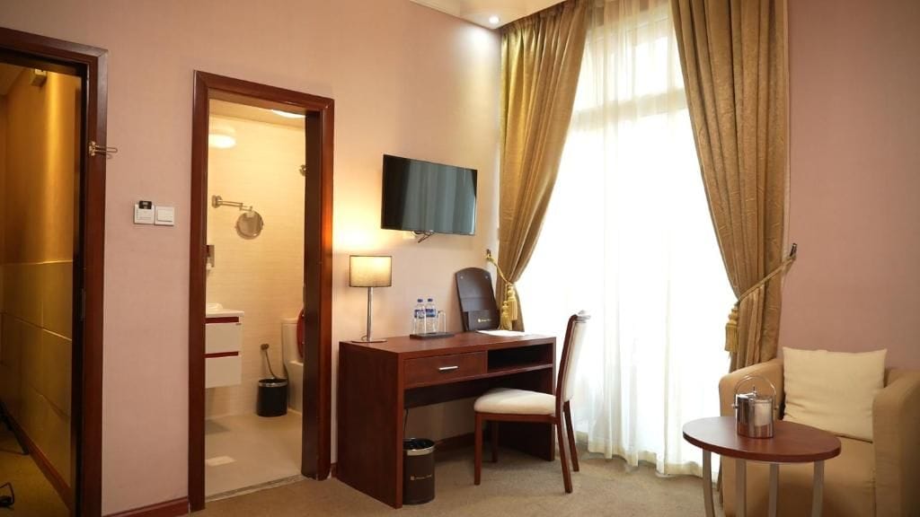 Habitación de hotel con escritorio, silla, televisor y una mesita con hervidor.