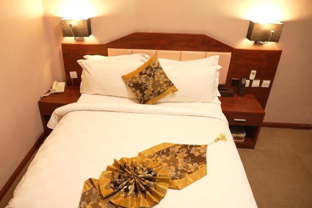Een hotelkamer met een opgemaakt bed, een nachtkastje met een lamp en een bijzettafeltje met een telefoon.