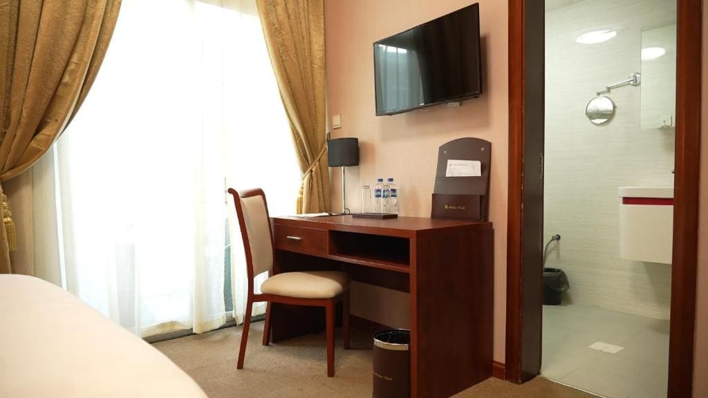 Habitación de hotel con escritorio, silla, televisión y zona de ducha de vidrio.