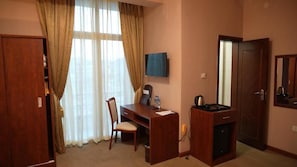 Habitación de hotel con un escritorio de madera, una silla, un televisor montado en la pared y una puerta con espejo.