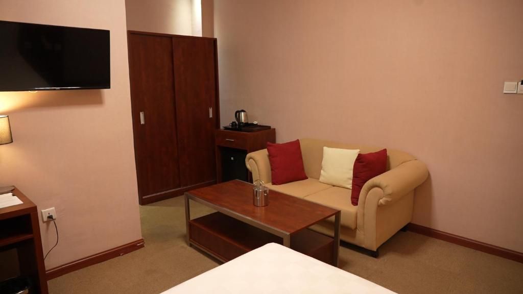 Ein Hotelzimmer mit einer Couch, einem Couchtisch, einem Fernseher, einem Kleiderschrank und einem Schreibtisch mit Lampe.