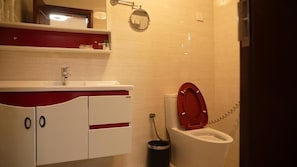 Un baño con un lavamanos blanco, detalles en rojo, un inodoro y un cubo de basura.