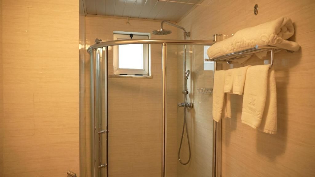 A glass-enclosed shower with a handheld showerhead, a towel rack with towels, and a small window above the shower.