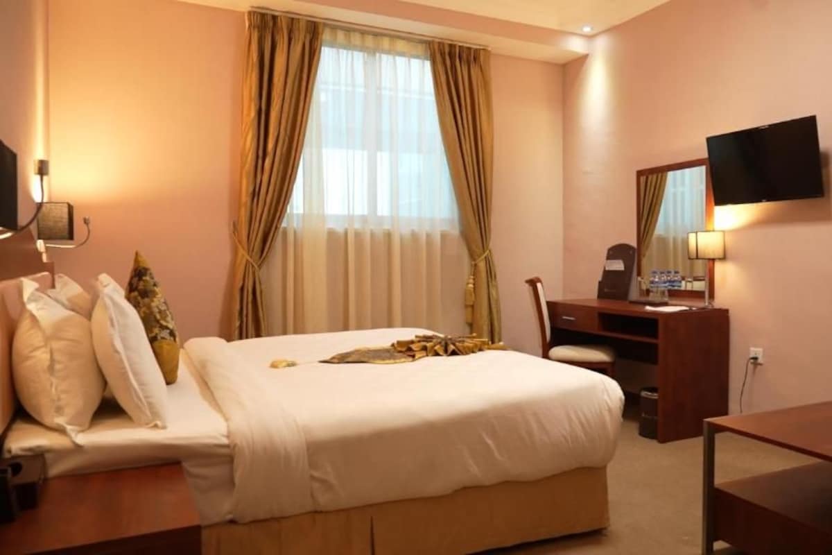 Een hotelkamer met een bed, bureau, stoel, televisie en gordijnen.