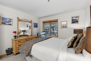 A bedroom with a bed, dresser, mirror, and a window with a view of a building. - Snowy Owl Lodge | Walk to Slopes & Shared Hot Tub (Breckenridge)