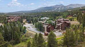 A mountainous resort area with multiple lodge buildings surrounded by dense forests and mountains in the background. - Snowy Owl Lodge | Walk to Slopes & Shared Hot Tub (Breckenridge)