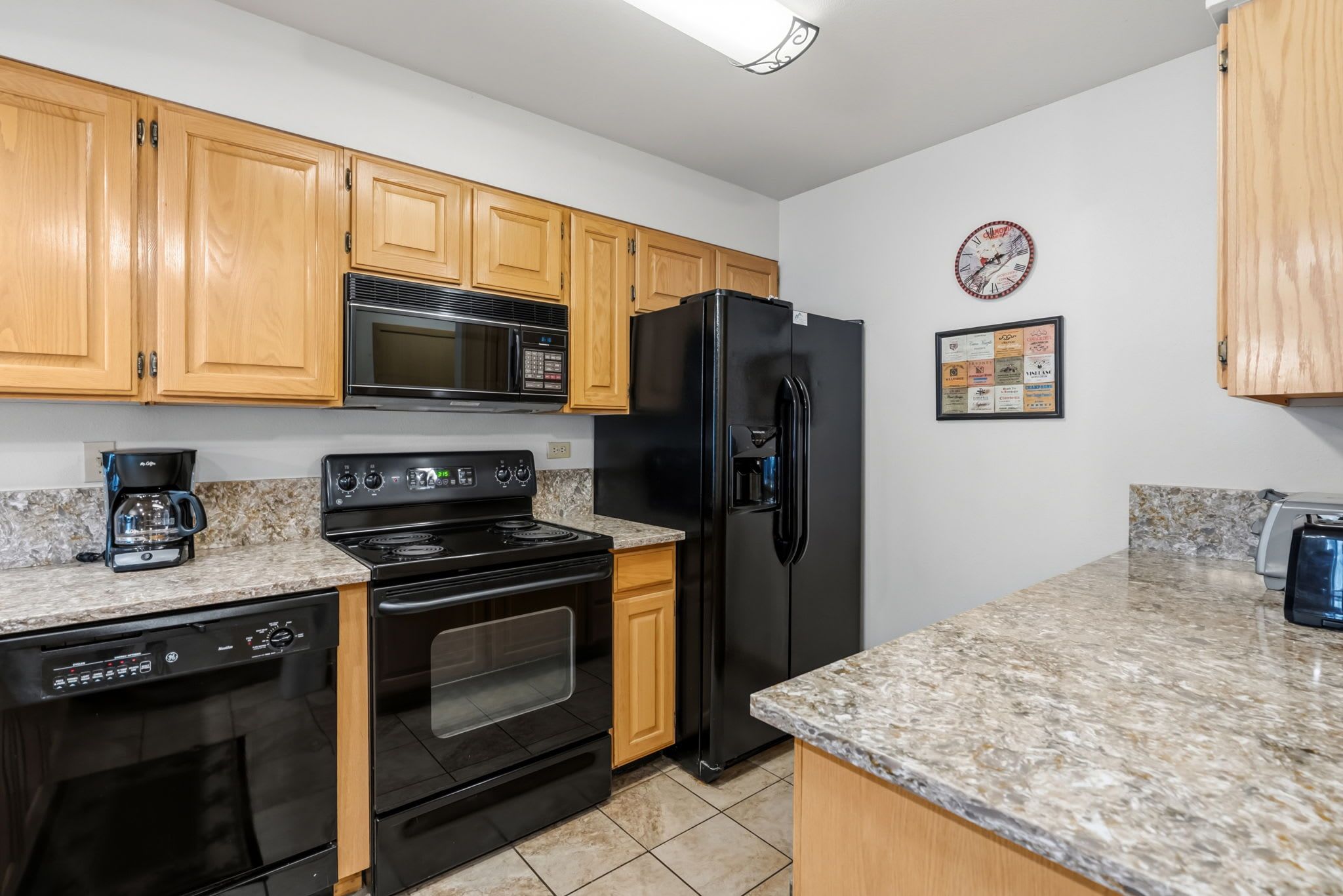 A kitchen with wooden cabinets, a black refrigerator, a microwave, a stove, and a coffee maker.