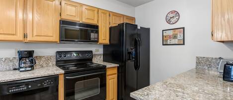 A kitchen with wooden cabinets, a black refrigerator, a microwave, a stove, and a coffee maker.