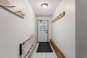 A narrow hallway with a white door, a black mat at the entrance, and a wooden handrail on the right. - Snowy Owl Lodge | Walk to Slopes & Shared Hot Tub (Breckenridge)