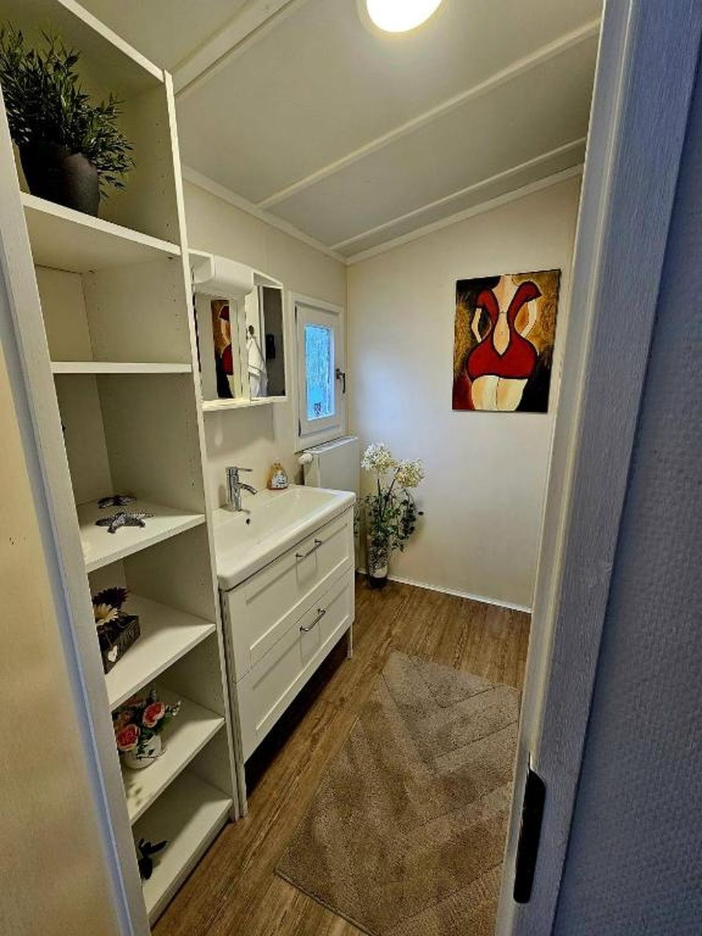 Une petite salle de bain avec un meuble-lavabo blanc, des étagères, un miroir et un tableau accroché au mur.